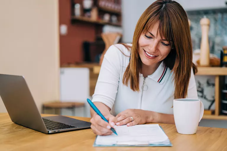 Woman with a laptop making notes on a sheet of paper.