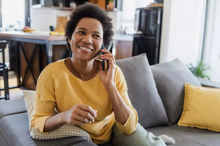 A woman sitting on a couch on the phone and smiling.