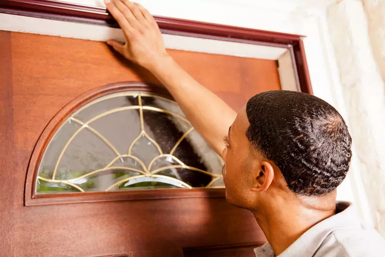 A man checks the top edge of a front door for gaps.