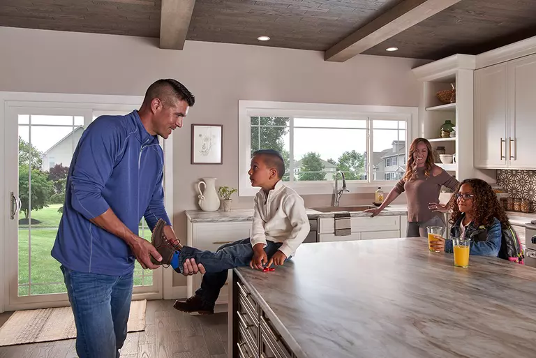 A father putting his son’s shoes on him, while his mom and sister watch.