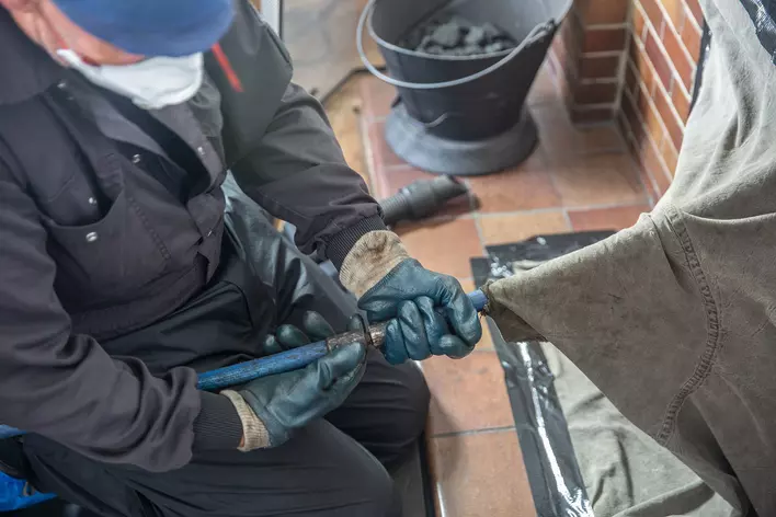 Chimney sweep cleaning a traditional open fire with face covering and protective
clothes.