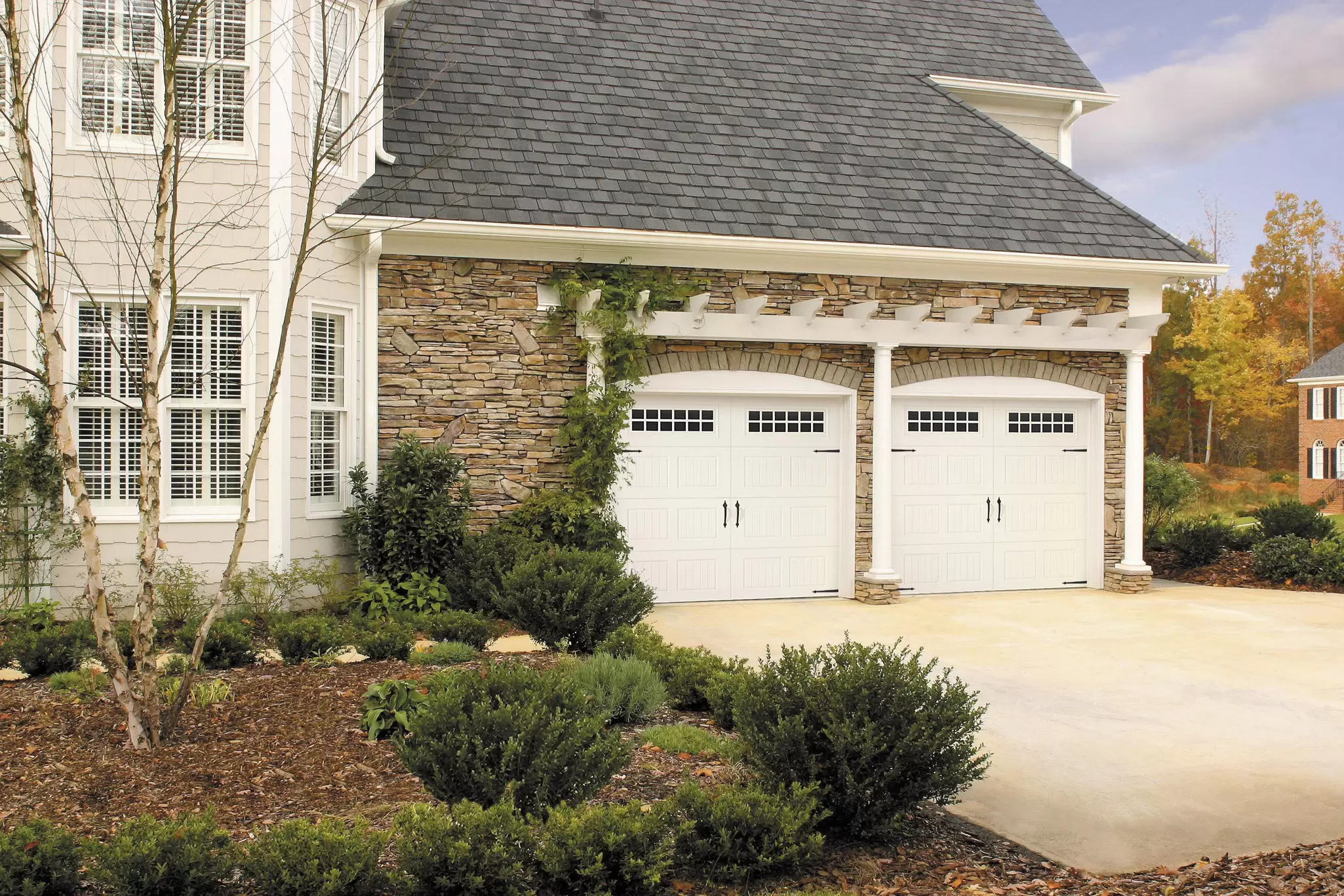 Two garage doors attached to a house surrounded by bushes.