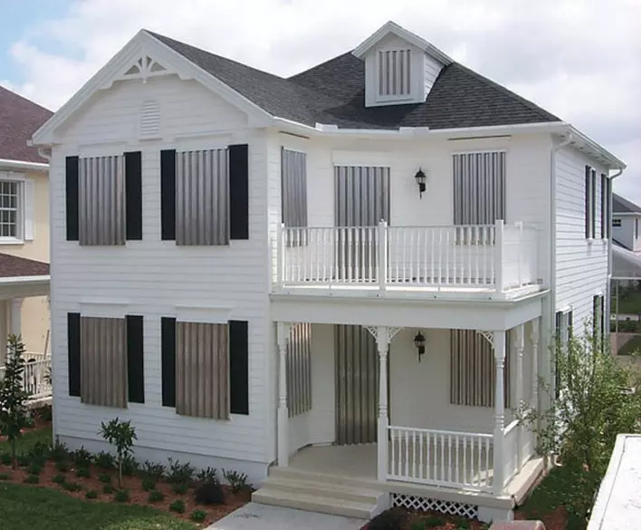 A white two-story house sporting hurricane panels.