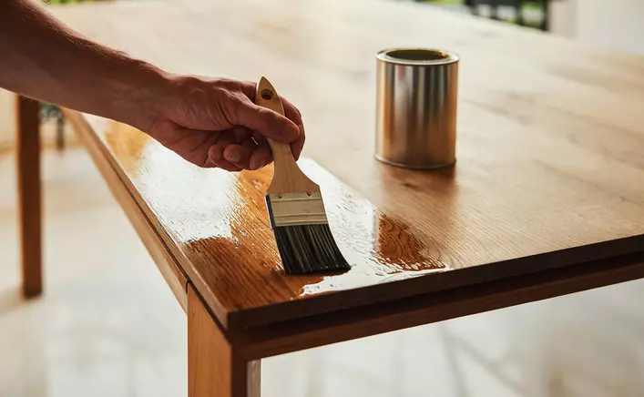 Someone sealing their wooden table to prevent sun damage.