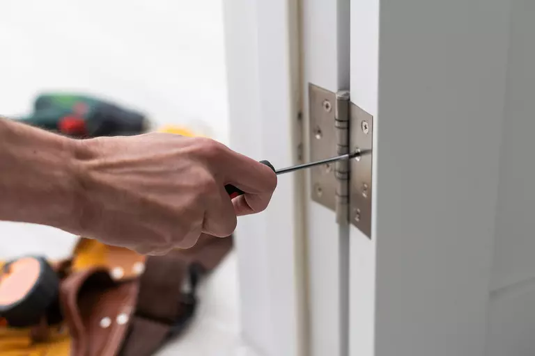 Person screwing nails into door hinges during an exterior door installation