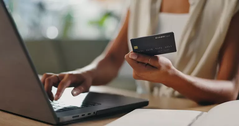Woman holding a credit card while typing on a laptop.