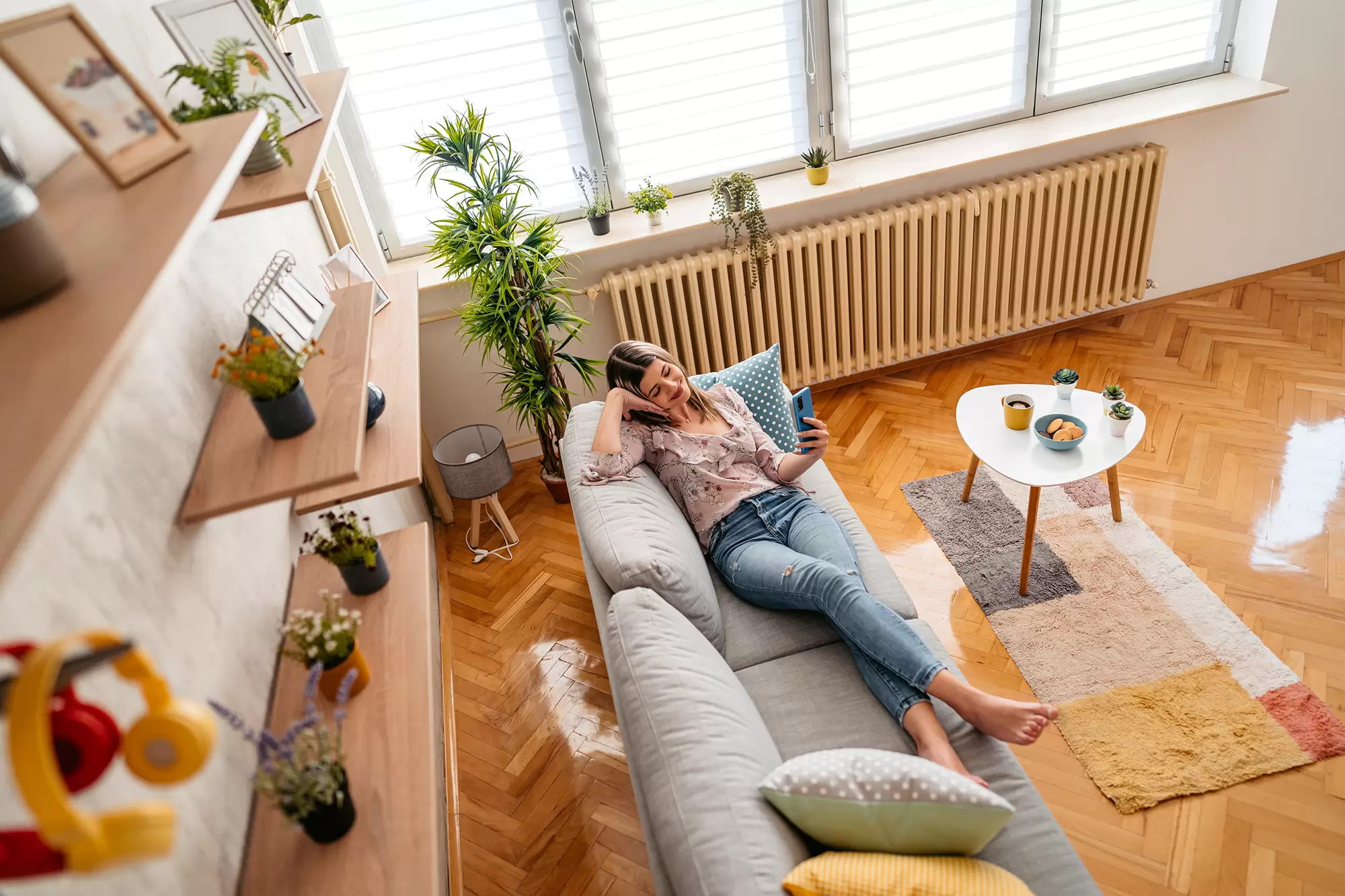 Woman on a living room couch next to sunlit windows.