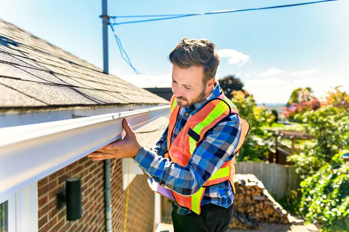 A contractor on a ladder carrying out a roof inspection on a home.