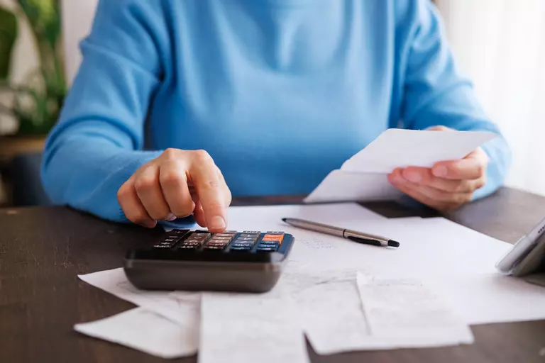 Individual doing calculations with pen, paper, and calculator.