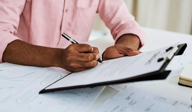Close-up shot of a man filling in paperwork on a clipboard in an office.