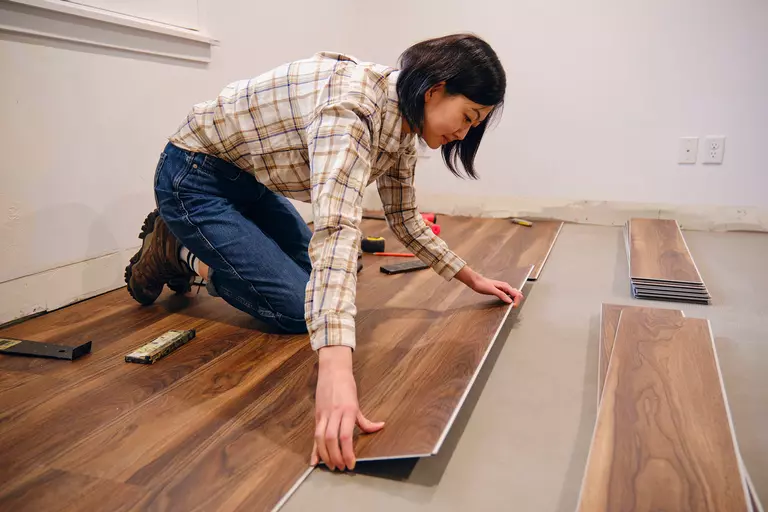 A woman laying down new hardwood floors herself during her home renovation.