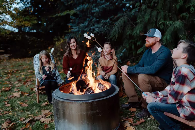A family gathered around a firepit in their backyard, roasting marshmallows together.