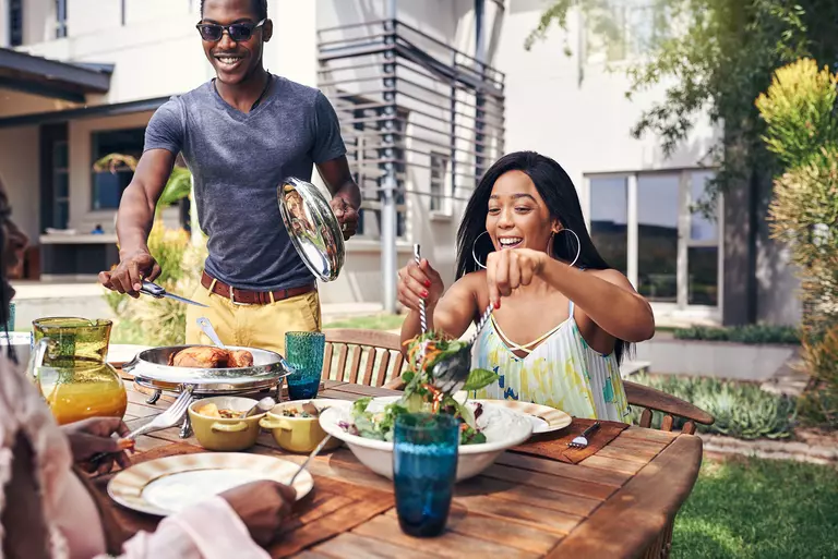 A family eating in their backyard dining area on a bright, sunny day.