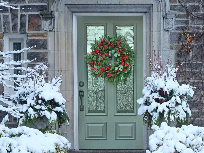 Front door with multi-pane glass and a Christmas wreath with red holly berries on an old
            stone-faced house