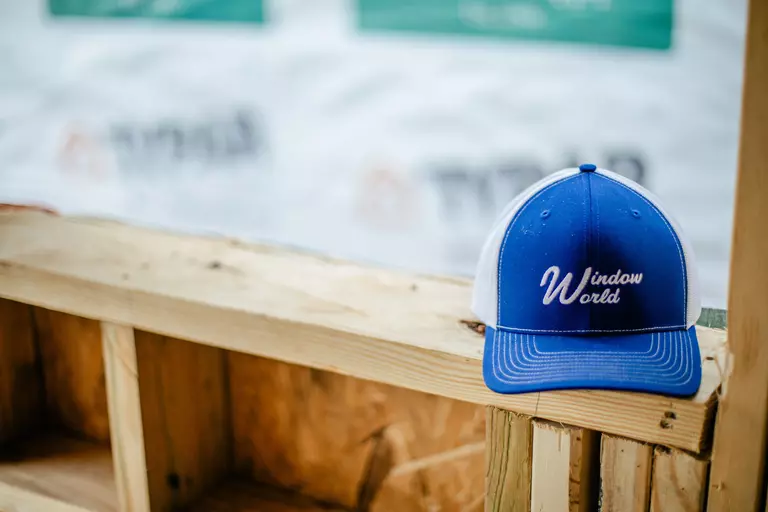 Close-up of a Window World blue and white branded hat sitting on top of a wooden frame.