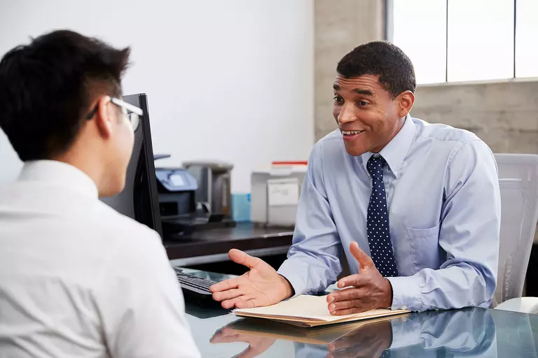 Man at a desk enthusiastically sharing information with another individual.