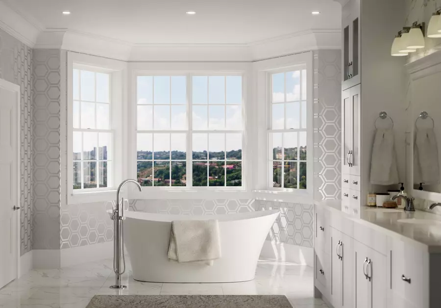 Picture of a brightly remodeled bathroom with a large bathtub in front of a set of white windows,