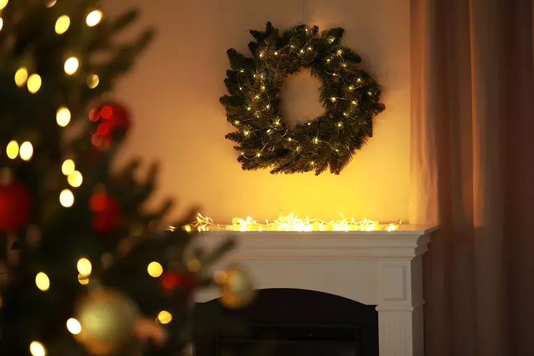 A Christmas wreath with holiday lights suspended over an unlit fireplace.