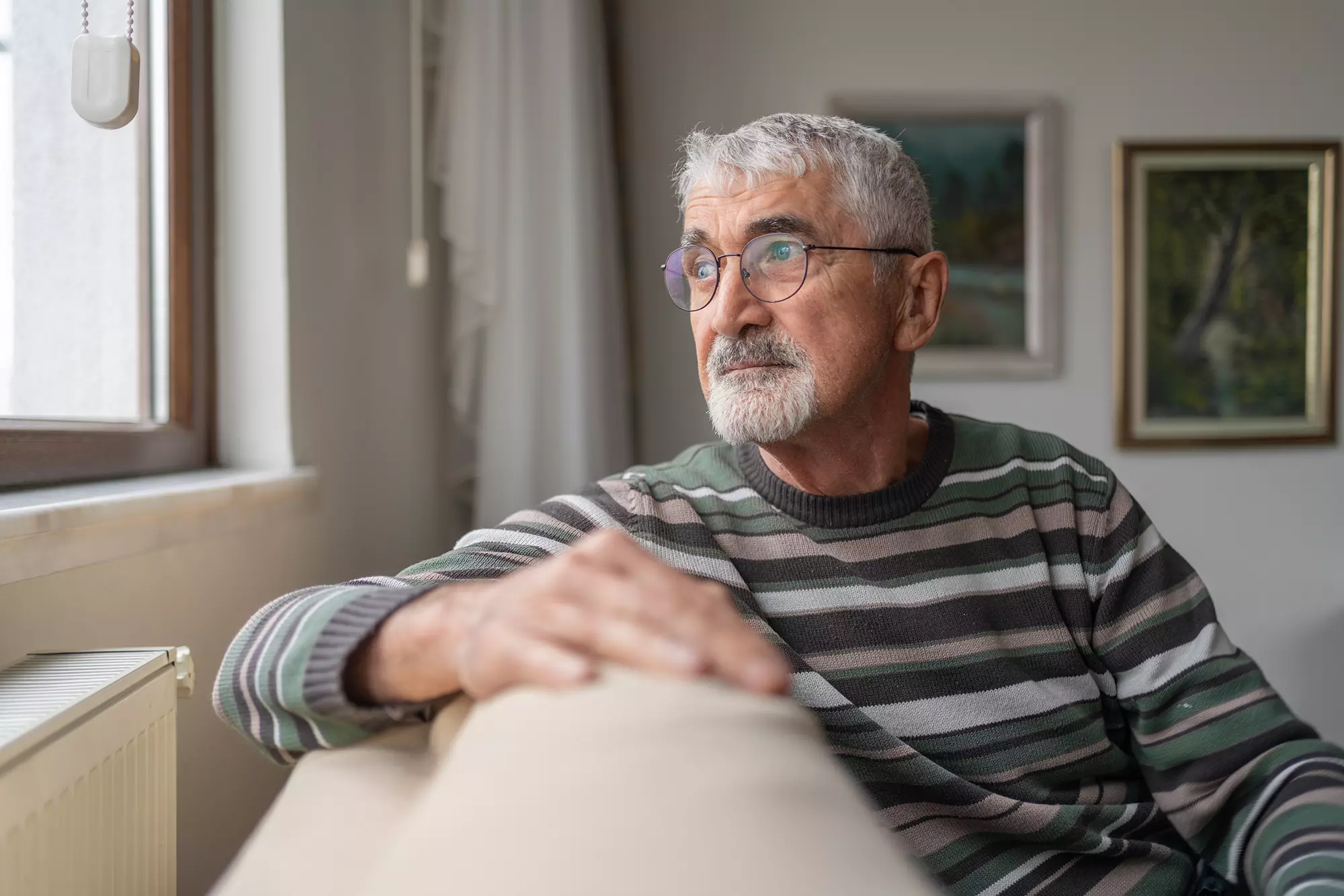 Older man sitting near a window with minimal natural light.