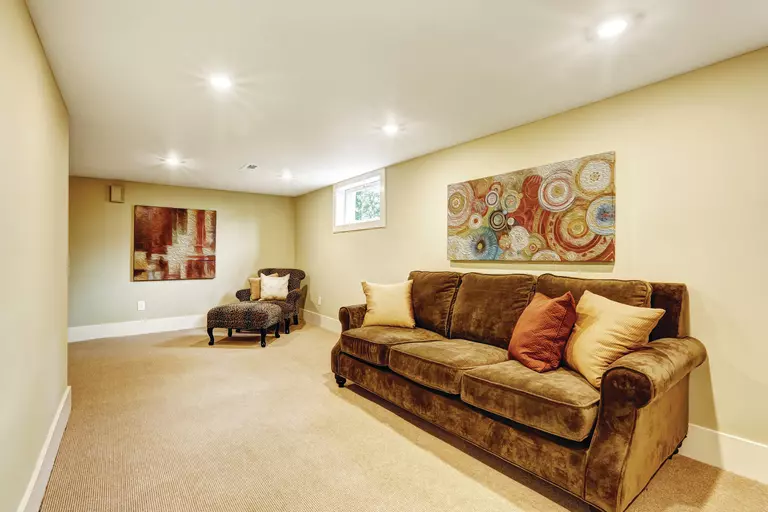 A living area in the basement of a home that allows natural light in through an awning window.