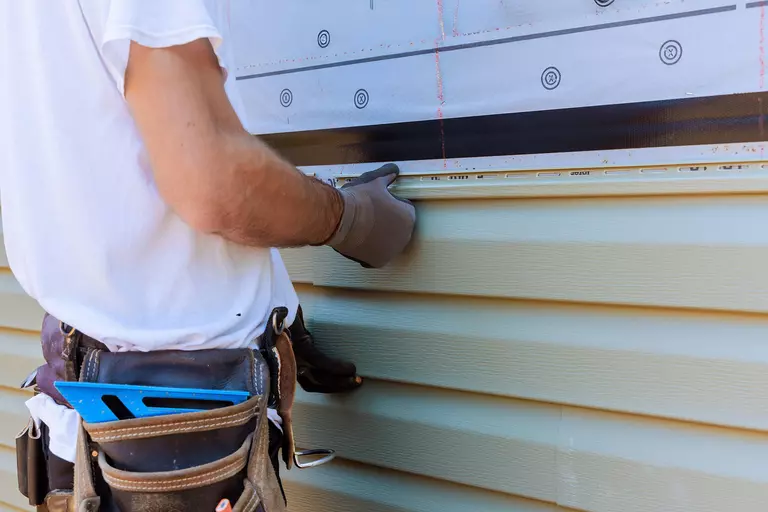 A man replacing a piece of vinyl siding.