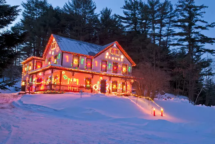 The exterior of a snow-covered home decorated with colorful Christmas lights on
gutters, window frames, and railings.