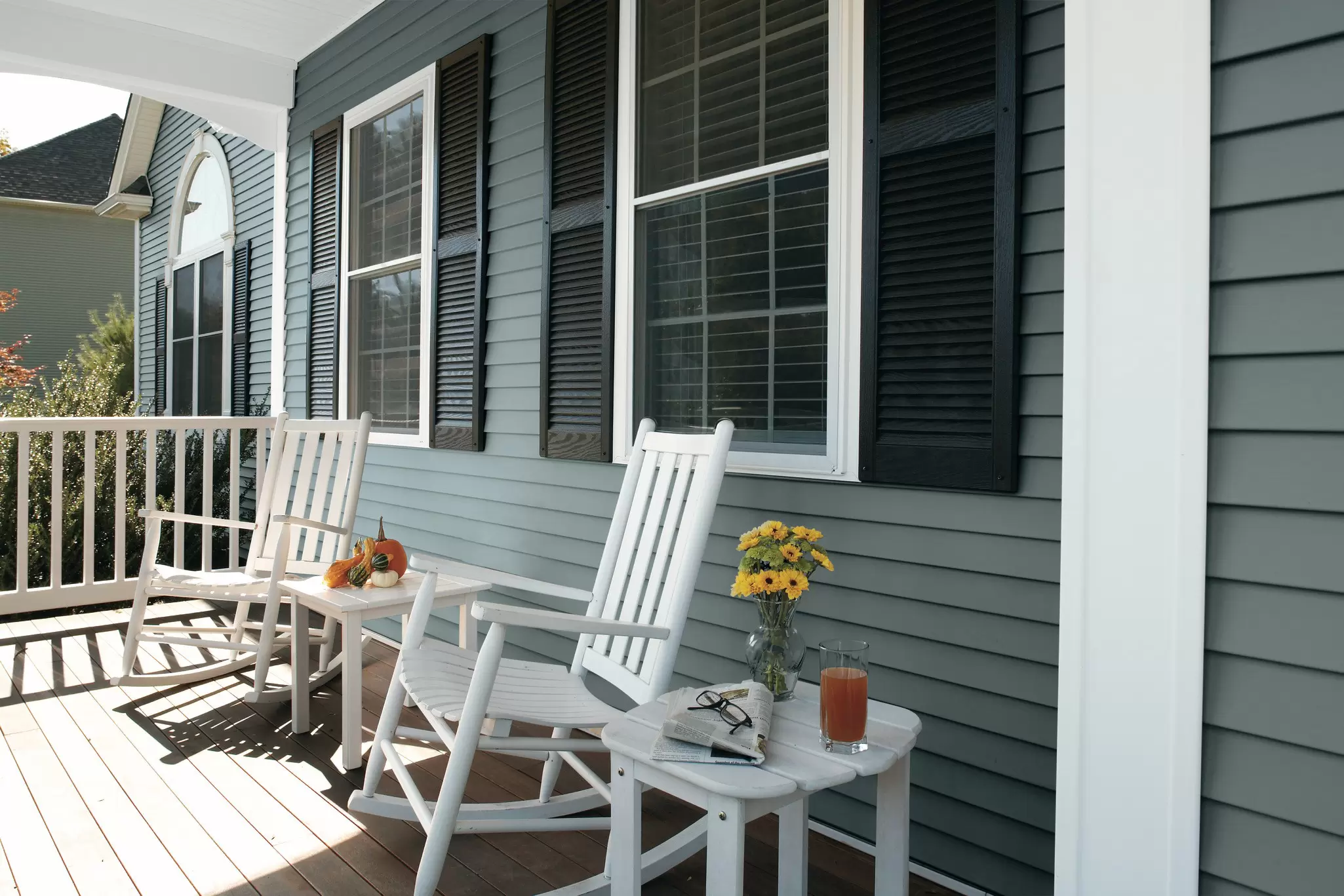 Front porch with white rocking chairs, blue horizontal siding, and windows with black shutters.