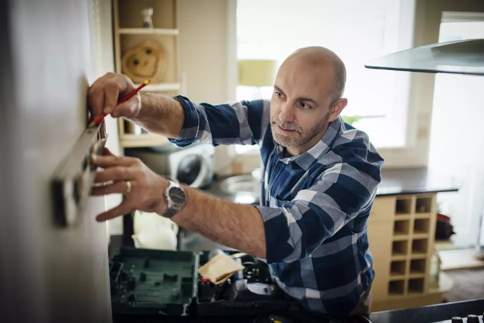 Mature man using a spirit level and marking the wall with a pencil in his kitchen