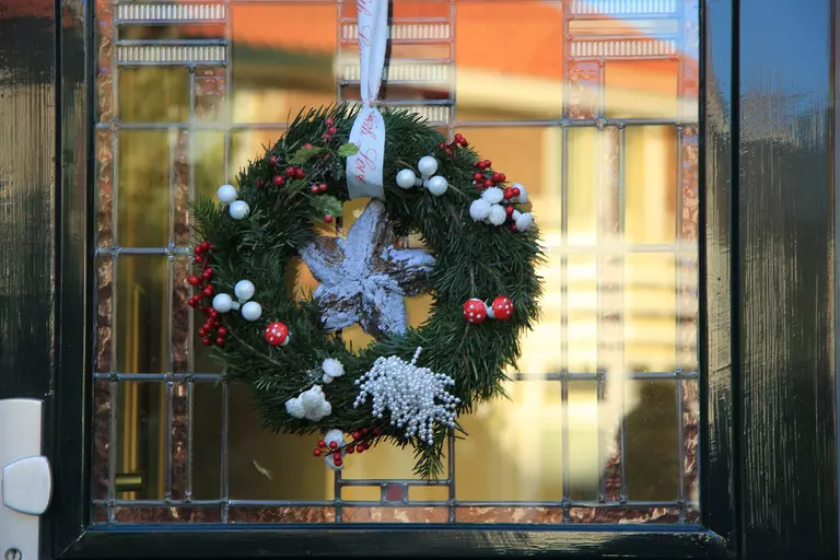 A wreath with foliage decorations hanging in front of a door from a white ribbon.