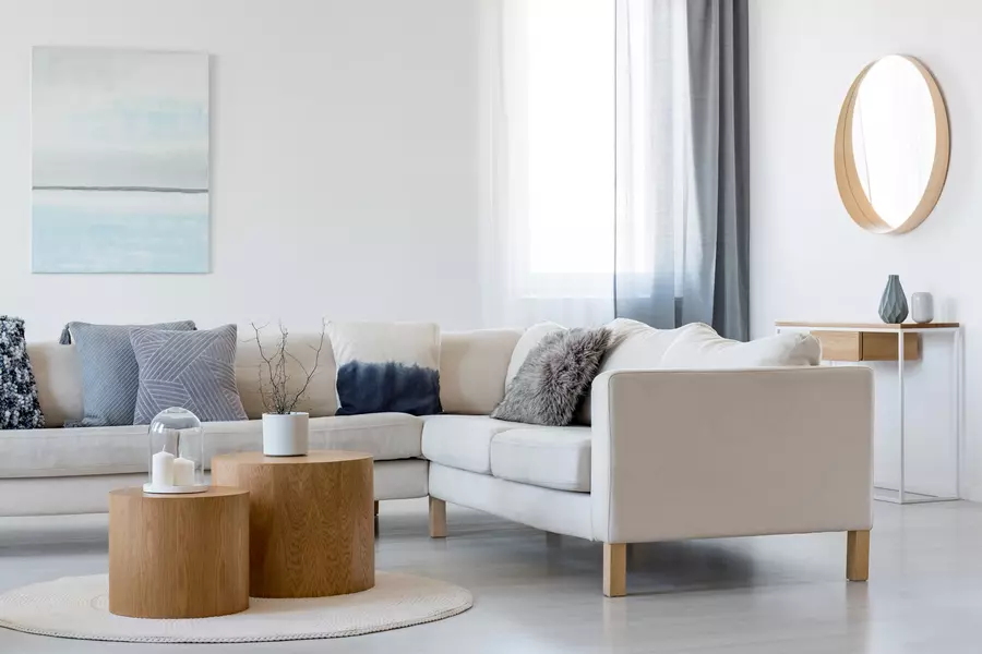 Cozy living room with a light gray sectional couch and one bright window 