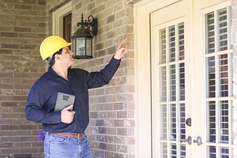 A man with a hard hat inspects the side of an exterior door for alignment.