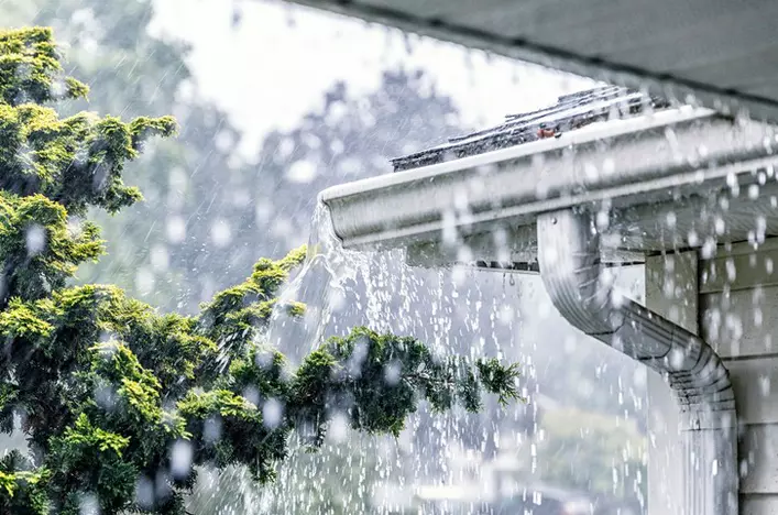 Rainstorm water coming down on a home with a gutter system attached to protect it. 