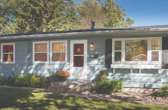 A blue ranch-style home with a white standard storm door on its entryway.