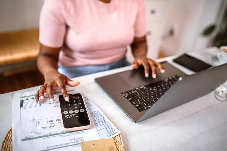 Woman managing finances using a smartphone calculator and a laptop.