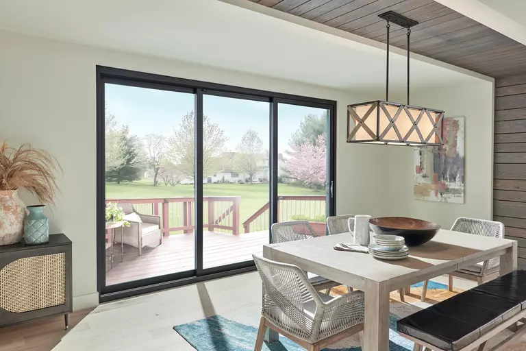 A black three-panel sliding patio door separating a dining room and a wooden deck.