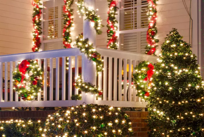 Light-up Christmas garland on a home’s exterior windows and railing, with bushes and
shrubs covered in lights.