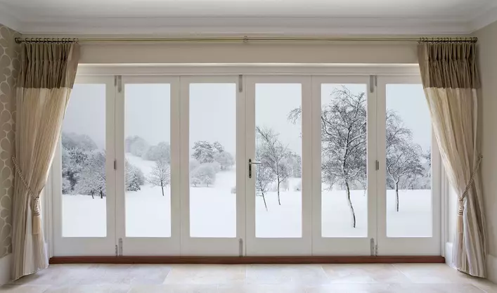 Accordion patio doors spanning across the entire length of a room overlooking a large plot of land covered in snow.