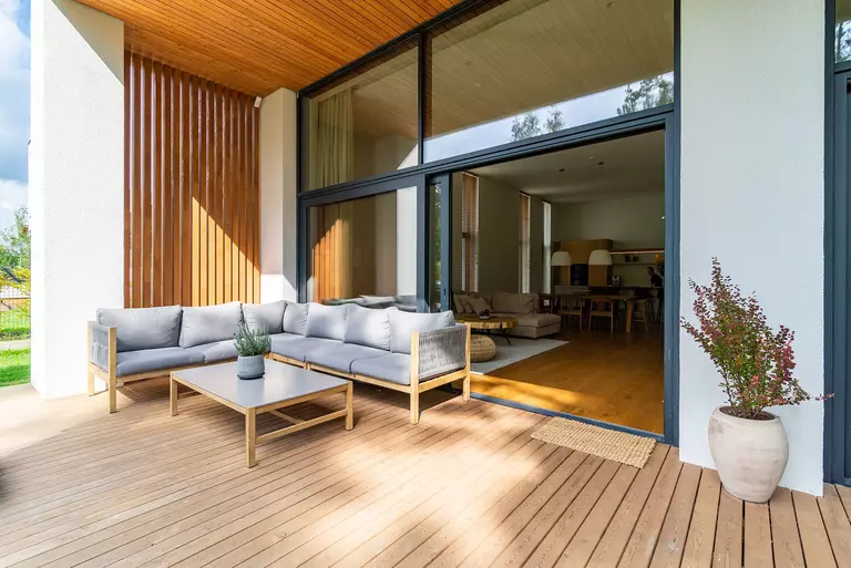 Cozy wooden patio and outside living space with a seating area next to an entrance to the house.