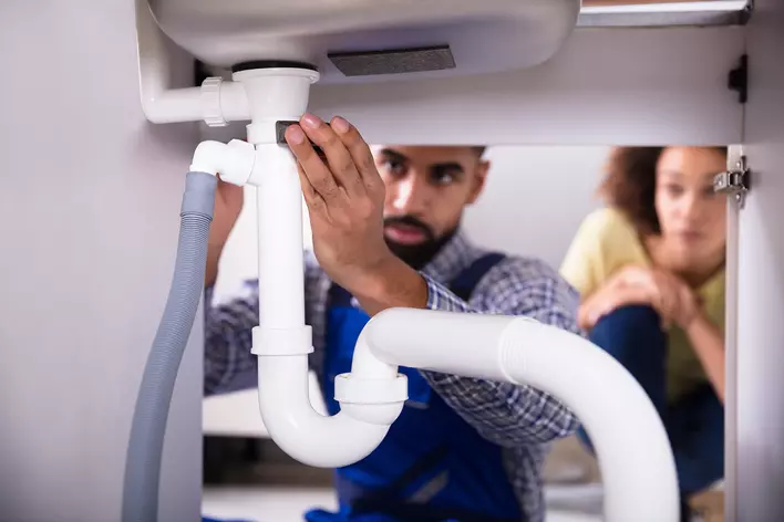 A technician fixing the water leak under the sink of a woman’s home.