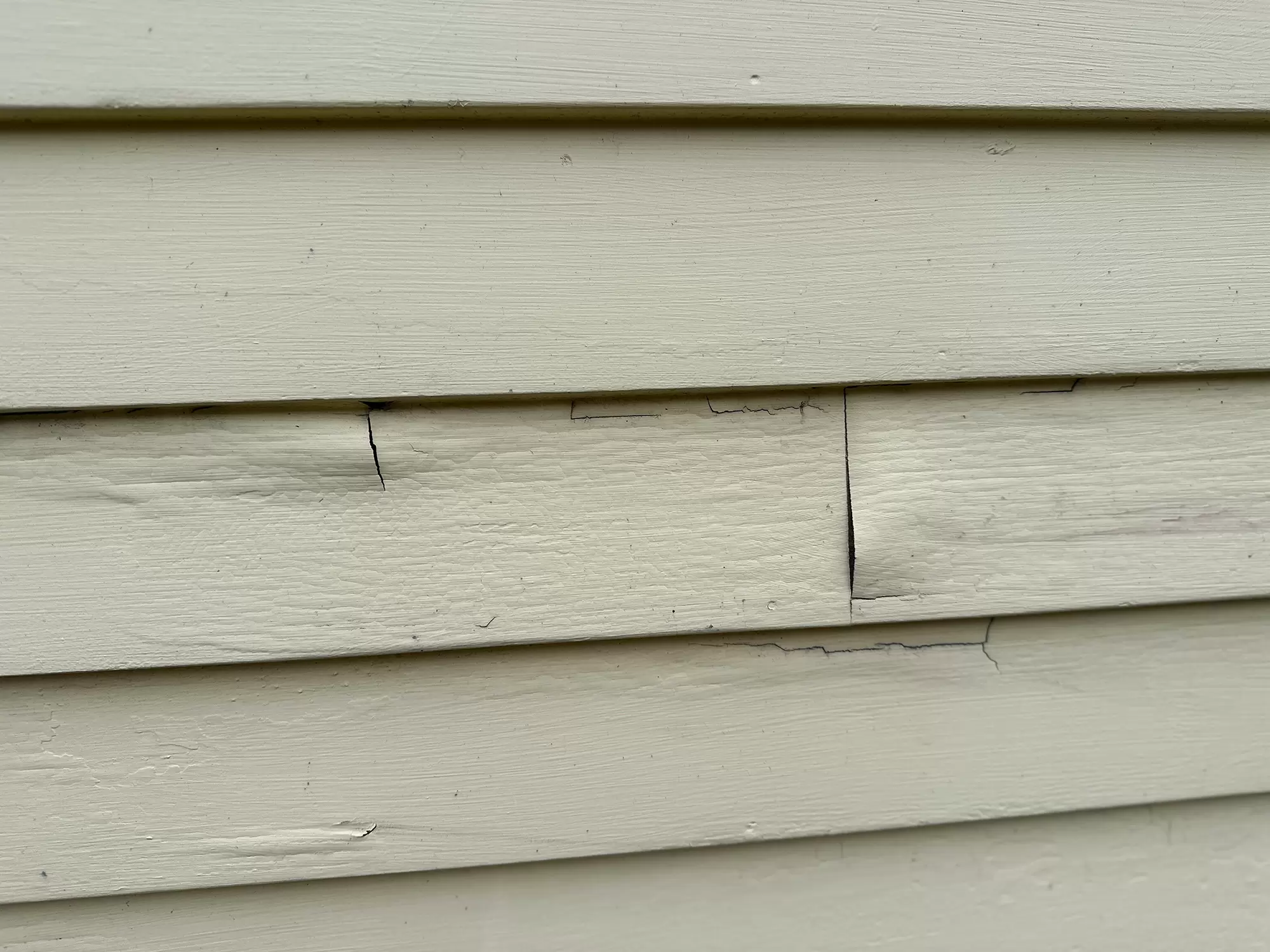 Cracked and weathered cream lap siding showing wear that signals it is time for replacement.