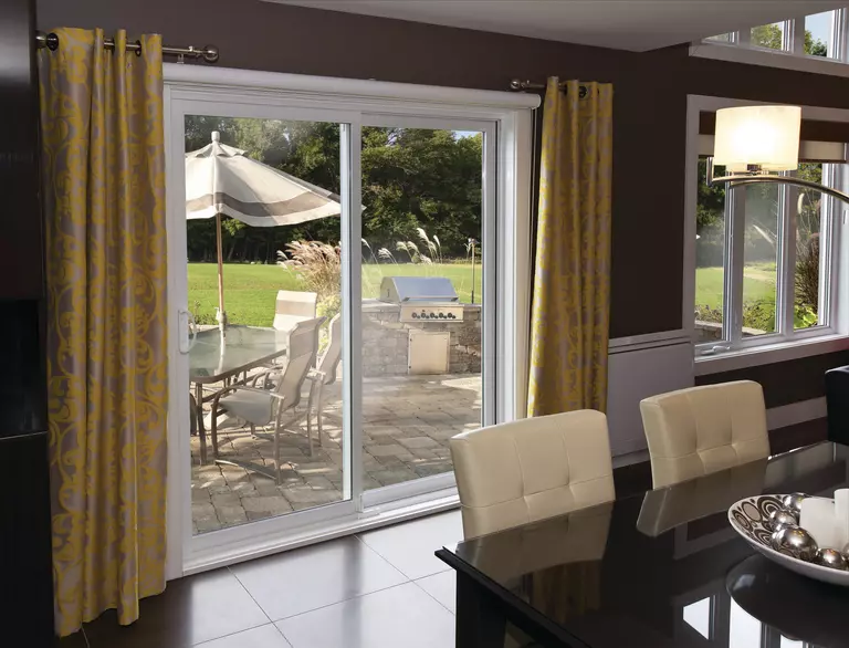 Dining room of a home with sliding patio doors showing the back patio with grill, table, and chairs.