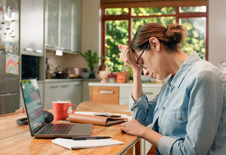 Woman stressed out across from laptop while sitting at table in kitchen of home.