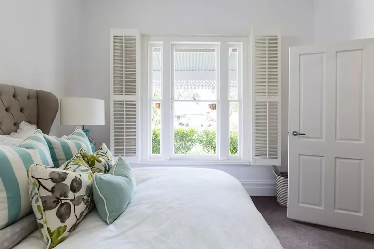 Bedroom of a home with white interior shutters around the bedroom window.