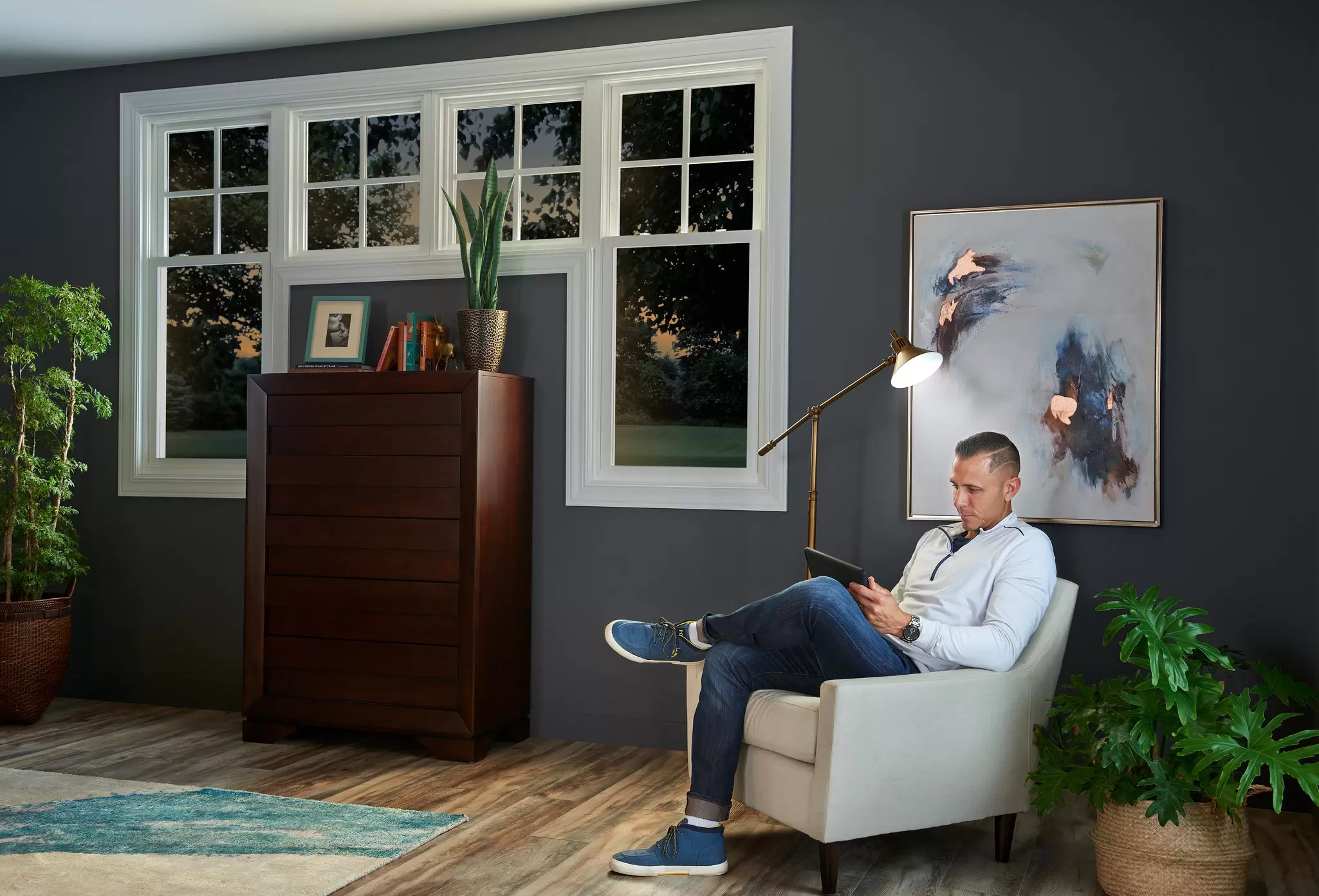 Man in a bedroom reading on a tablet device next to custom windows.