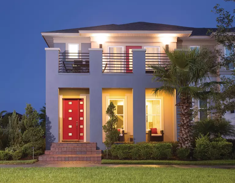 A gray stucco multi-level home with a large red steel entry door and a red patio door on the second-level balcony.
