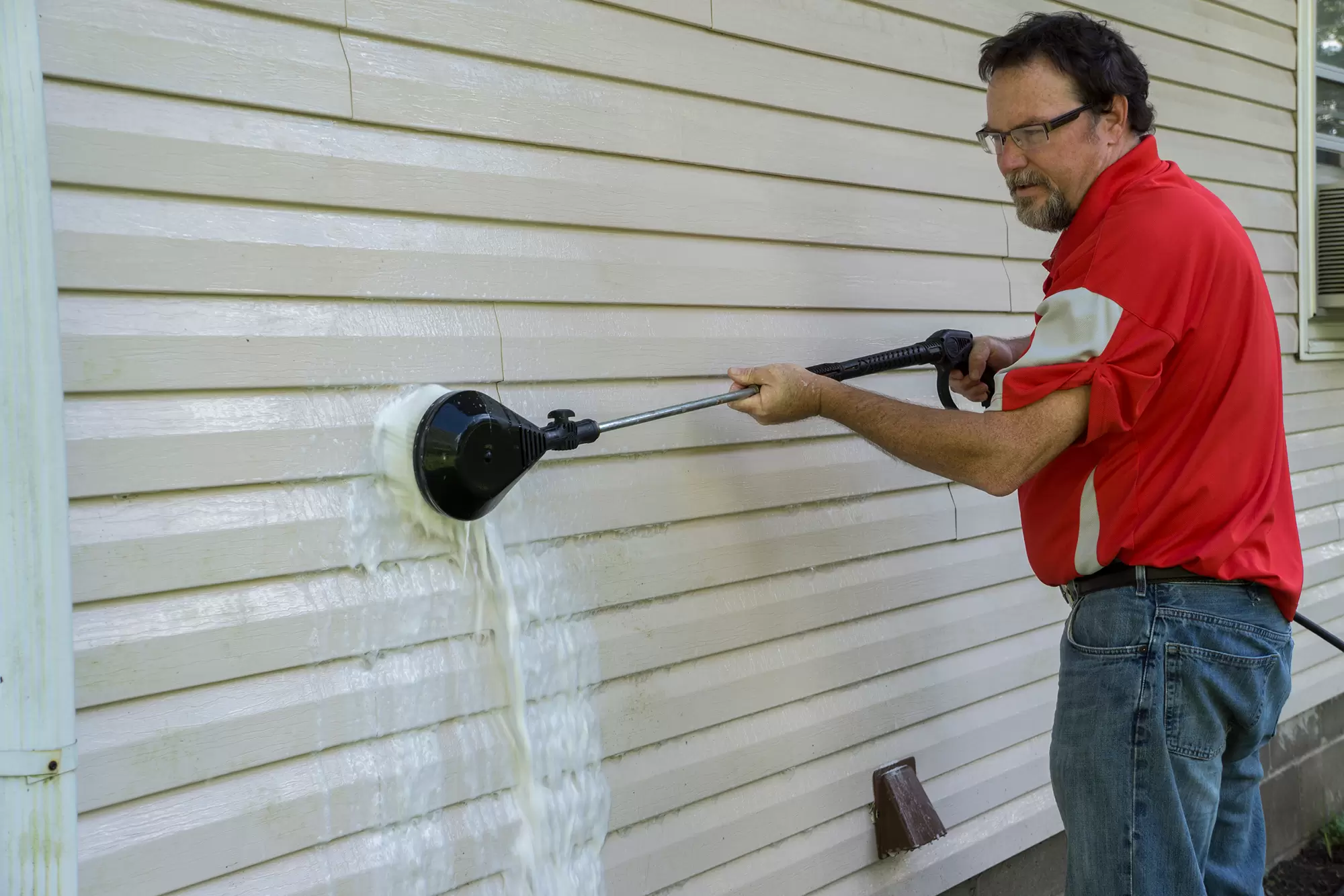 Man pressure washing vinyl siding on a house exterior.