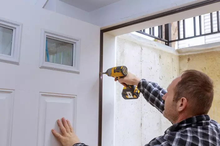 A person screwing the hinge of a door with a screwdriver  