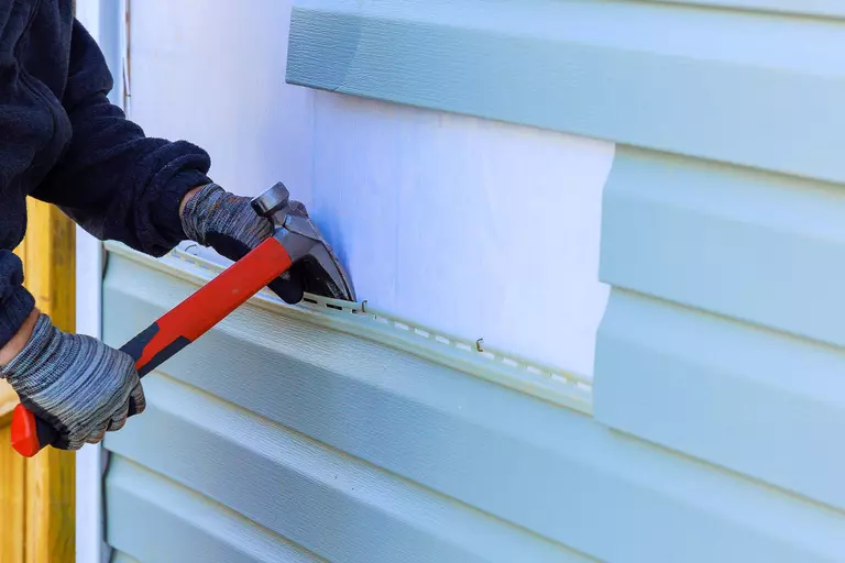 A worker removing vinyl siding from a home with a hammer.