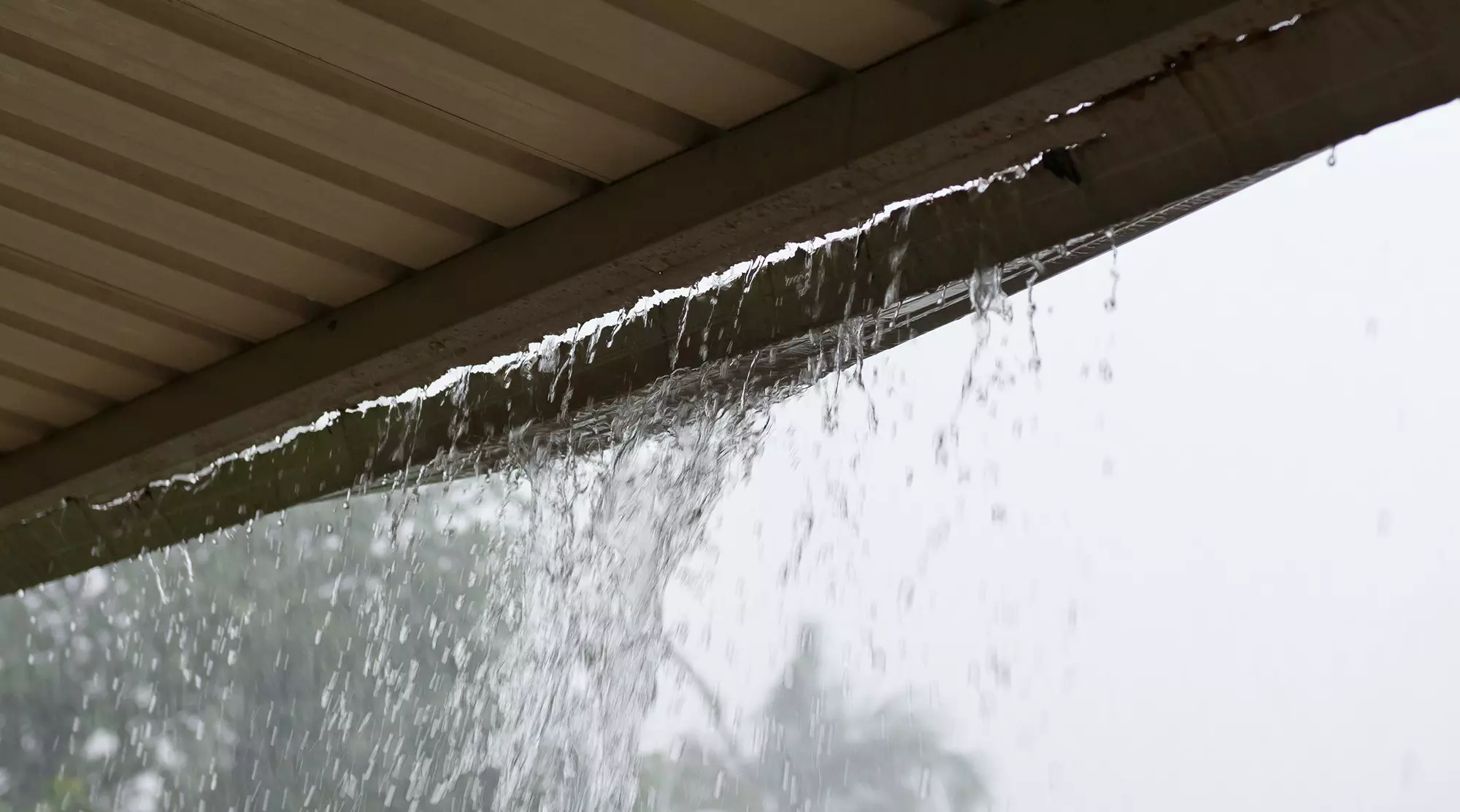 Water falling through the gutters onto the porch of a home, indicating gutter holes and leaks.