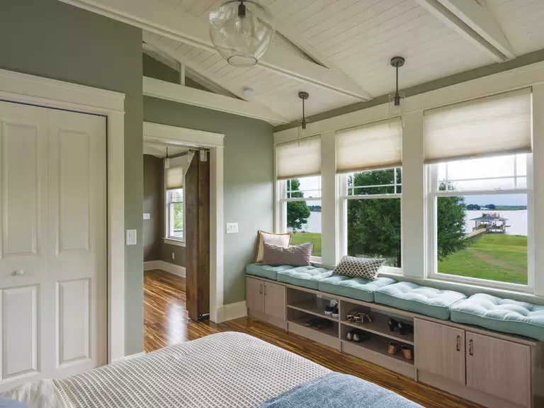 A bedroom with a lake view through three double-hung windows.